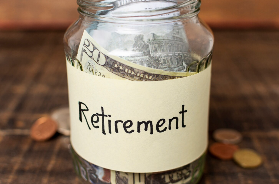 Glass jar labeled retirement filled with cash savings and coins on a wooden table