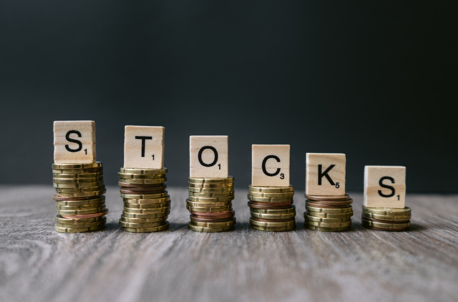 Stacks of coins with wooden letter tiles spelling “STOCKS,” symbolizing investment and wealth building.