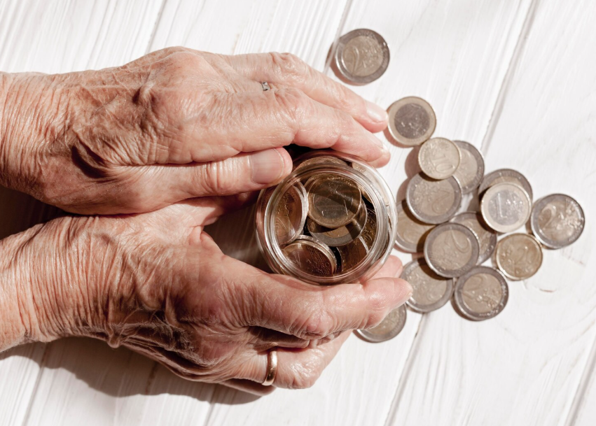 Elderly hands holding a glass jar filled with coins, symbolizing saving money for retirement.
