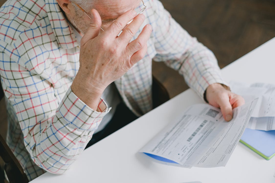 Stressed senior man holding bills while reviewing financial expenses at home