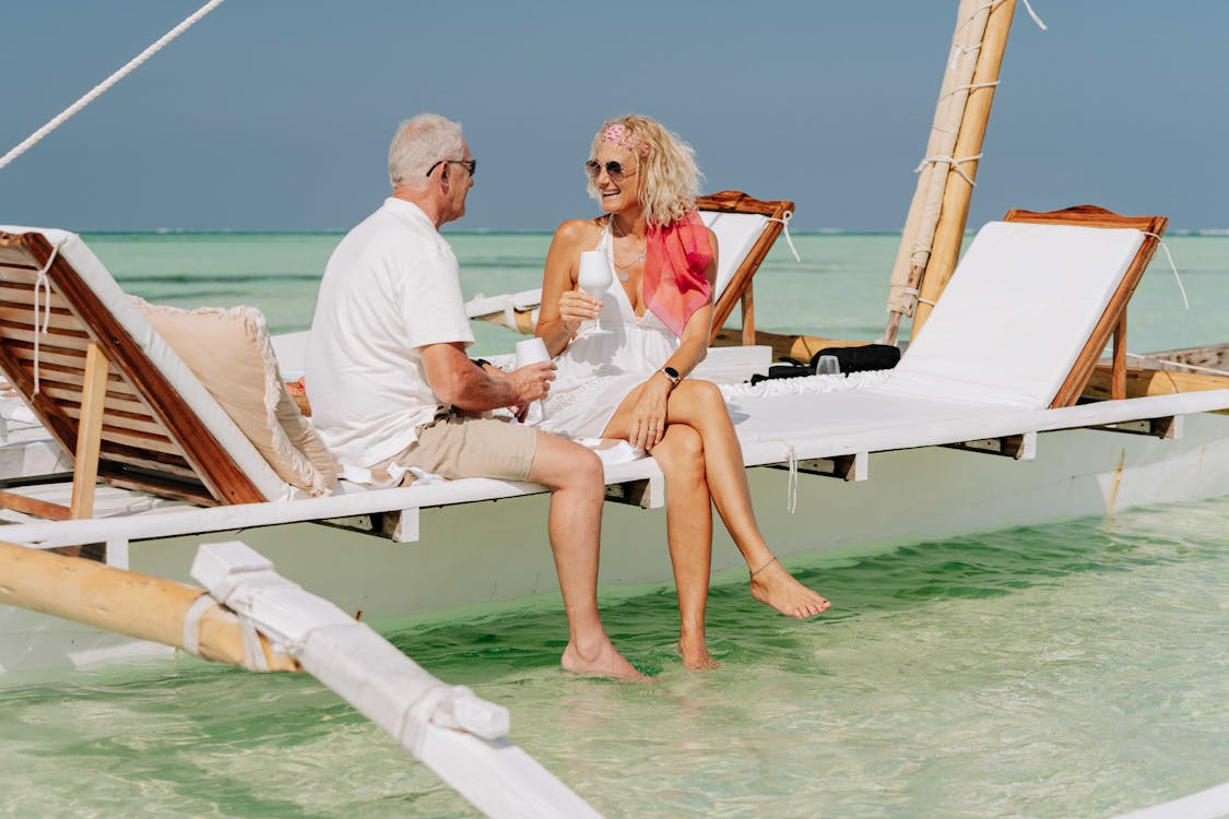 Happy retired couple relaxing on a beach lounge chair in the ocean, enjoying a bucket list vacation experience.